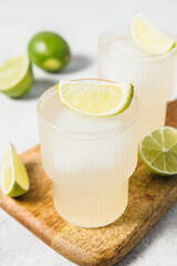Refreshing lime cocktails on wooden board. Two glasses of citrus hard seltzer with ice cube and...