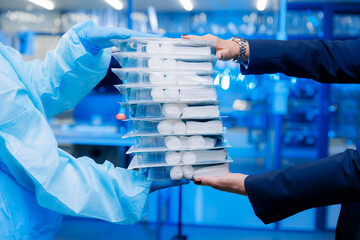 Concept purchase of medical equipment and protective equipment vs virus. Businesswoman and doctor in protective suit holds sterile kits for surgery operations on blue factory background