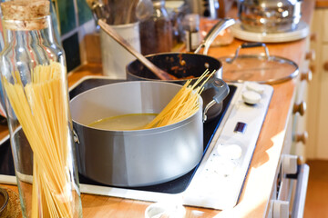 Cooking pasta in a home kitchen interior the pan has boiling water to cook spaghetti and raw ingredients on the kitchen counter