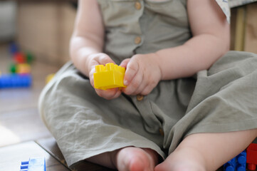 Child is sitting on warm floor, there are constructs around him, in hands of toddler is piece of plastic constructor, close up. Concept play, creativity, development fine motor skills, logic