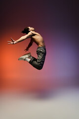 A young African American male dancer jumps in mid-air, arms outstretched, against a colorful gradient background.