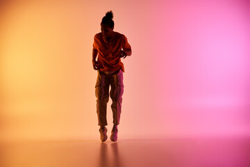 A young African American man dances on a colorful background, illuminated by neon lights.