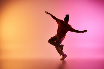 A young African American male dancer executes a move in a vibrant studio setting with a colorful gradient background.