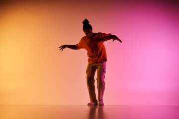 An African American male dancer performs a dynamic move against a gradient backdrop of vibrant yellow and pink lighting.