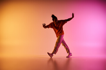 A young African American man in a casual outfit dances expressively against a vibrant gradient background of yellow, orange, and pink.