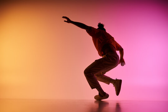A young African American man dances against a vibrant gradient background. He is captured in mid-air, showcasing his dynamic movements.