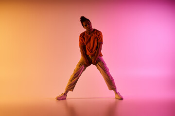 A young African American male dancer strikes a pose in front of a gradient background of yellow,...