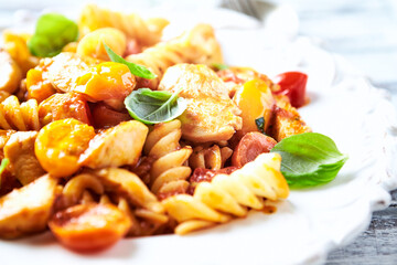 Pasta with chicken breast, cherry tomatoes and fresh basil. Bright wooden background. Close up.	
