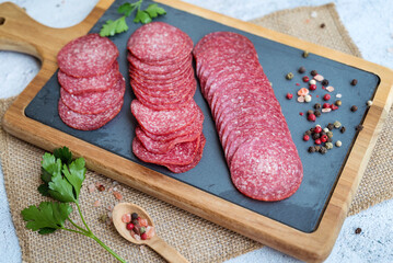 Wooden board with slices of tasty salami on light background