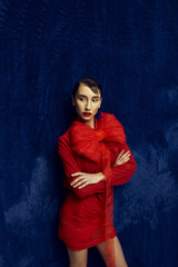 A young woman with short hair poses in a red dress and bow against a blue background.