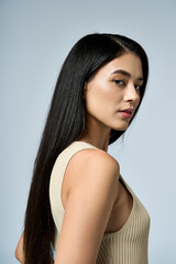 A young woman with long, dark hair poses confidently in a cream-colored tank top.