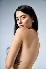 Fototapeta premium Young woman in studio with long black hair, back to camera, gazes over shoulder.