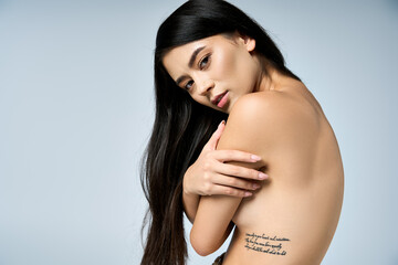 Young woman with long black hair poses, displaying ribcage tattoo.