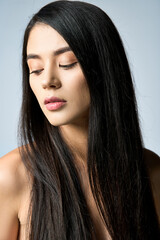 A young woman with long black hair looks down with a serene expression.