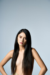 Fototapeta premium A young woman with long black hair poses confidently against a light blue background.
