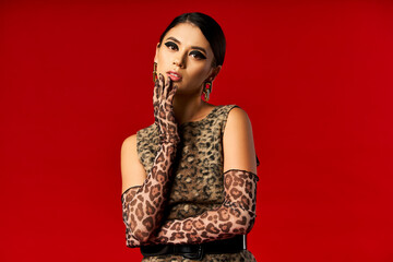 A young woman in a leopard print dress and gloves poses against a red background.