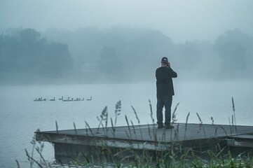 Man standing on a dock by a foggy lake in the early morning