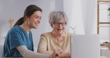 Empowering seniors. Friendly young nurse is patiently teaching elderly woman how to use laptop and health programs installed on it. Concept of medicine and technological adaptation among elderly.