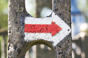 Hiking trail arrow. Red color paint guide arrow. Walking path indicator. Sign showing the way. Concrete pole next to the road.