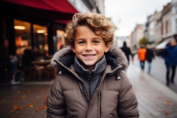 Fototapeta premium Outdoor portrait of cute little boy with blond curly hair, wearing warm coat, looking at camera and smiling.