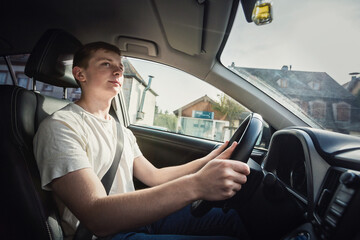 Side view young man driving car confident. Teenager driver enjoying the ride on the city street, keeps hands on the steering wheel looking focused at traffic