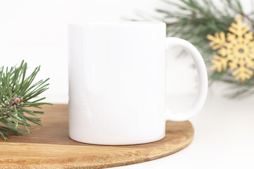 Christmas mockup of white coffee mug on wooden tray with pine branches and snowflake decoration. Blank 10 oz cup mug mock up for new year and winter holidays.