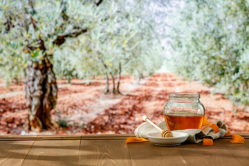 Glass jar of honey on wooden table with an alley of green trees in the park background. Space for advertising products.