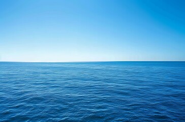 Obraz premium wide shot of the vast, calm sea under a clear blue sky. The water is a deep ocean color with gentle ripples and small waves in its distance