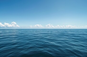 Fototapeta premium wide shot of the vast, calm sea under a clear blue sky. The water is a deep ocean color with gentle ripples and small waves in its distance