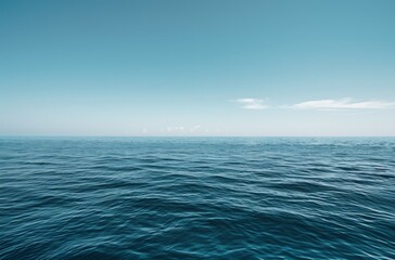 Obraz premium wide shot of the vast, calm sea under a clear blue sky. The water is a deep ocean color with gentle ripples and small waves in its distance