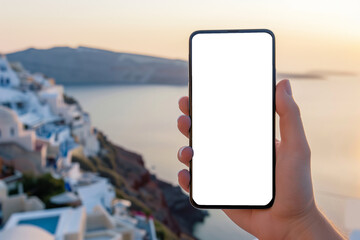 A close up of a man's hand holding a smartphone with a white mock up blank white screen and a town at sunset in the background