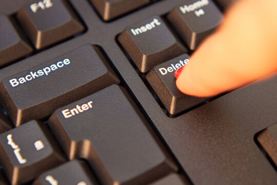 Close up em dedo feminino apertando a tecla "delete" em teclado preto de um computador.