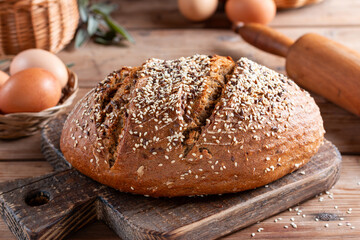 Rustic grain bread with oats, flax seeds, sunflower seeds and sesame seeds on a cutting board with a rolling pin on the background