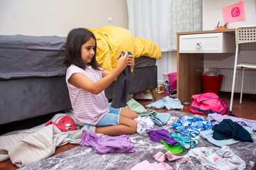 Little girl folding clothes in her messy room