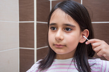 Little girl cleans her ear with cotton swab in the bathroom