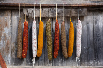 Variety of colorful cured sausages hanging against wooden backdrop