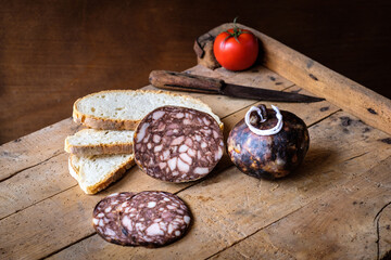 Assorted cured meats with bread and tomato on rustic wooden board