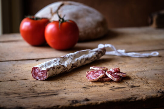 Sliced cured sausage with tomatoes and bread on rustic table - Powered by Adobe