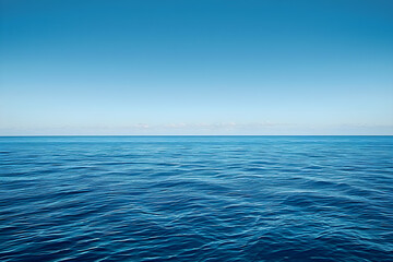 Obraz premium A vast expanse of deep blue sea with a horizon line stretching across an endless sky of clear and unbroken light blue color. Suitable for backgrounds and travel themes. Copy space.