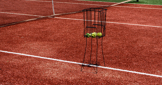 Empty tennis court with ball cart and vivid red surface