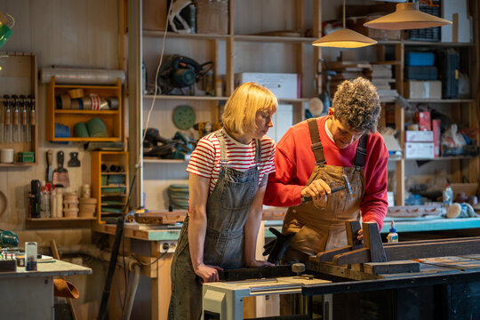 Woman, man working in carpentry workshop. Apprentice girl watching process of master work driving nails, making furniture. Female beginner, trainee and male professional manufacturing wooden products