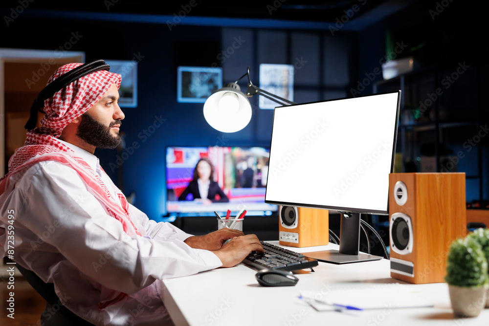 Poster islamic guy sits at his home office table, his desktop computer monitor displaying a blank white scr