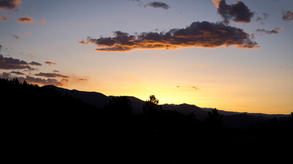 Beautiful color landscape photo of a mountain range silhouetted by a vibrant orange and red sunset with a partially cloudy sky and copy space.