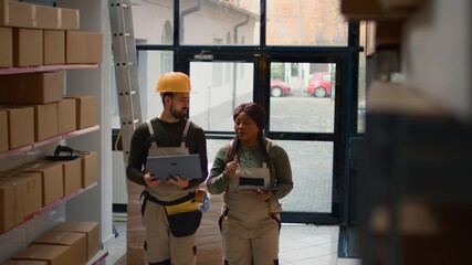 Precise workers preparing warehouse orders for delivery, using laptop and tablet to verify shipping...