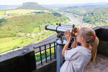 Cute curious kid girl observing Saxon Switzerland national park landscape with coin-operated...