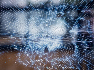 A shattered glass with a blue and white background. Surface is cracked. Act of vandalism and anti social behavior.