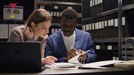 Multiethnic team of private detectives conducts a discreet inquiry, analyzing evidence and investigating records. Caucasian and african american investigators collaborate in office to solve crimes.