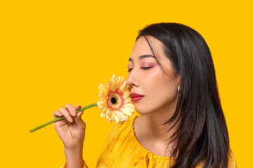Fototapeta premium Beautiful young Asian woman with gerbera flower on yellow background