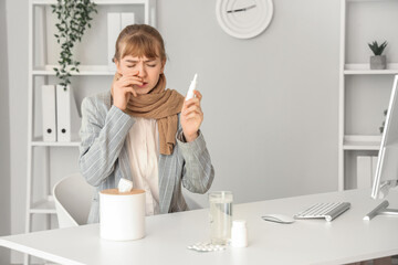 Ill young businesswoman with scarf and nasal drops in office