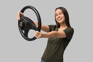 Beautiful young woman with steering wheel on grey background